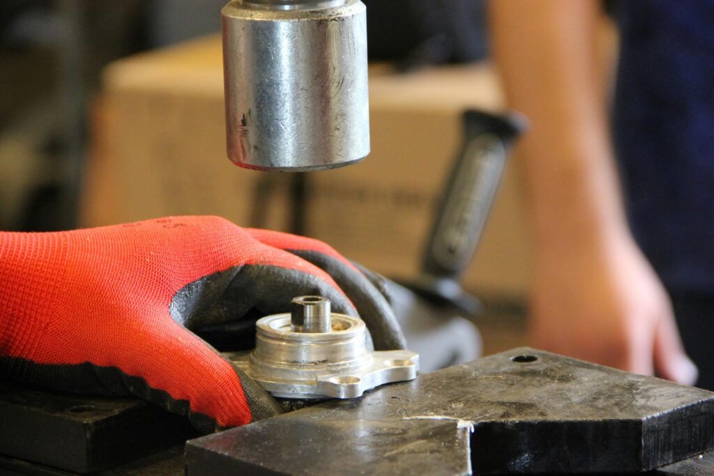 Hands in red gloves operate metal machinery in workshop close-up.
